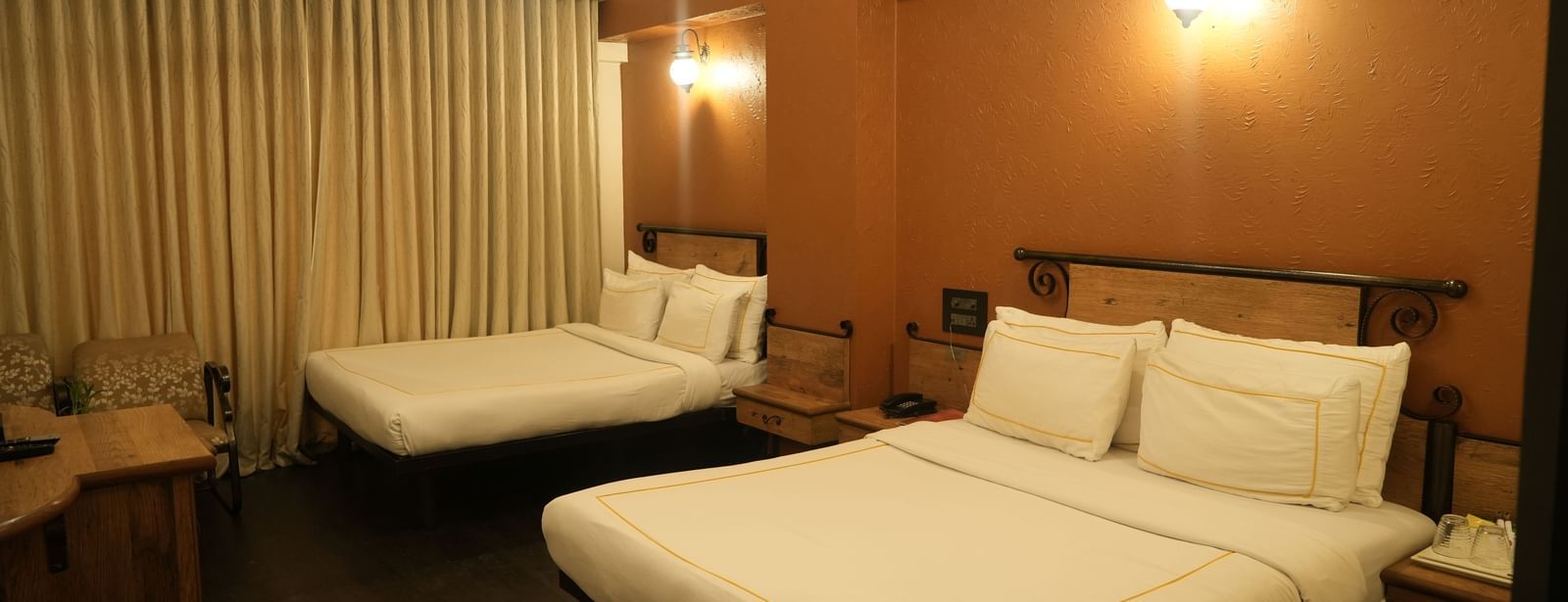 Bedroom with two double beds, curtains and warm lighting at Infiniti Hotel, Indore.