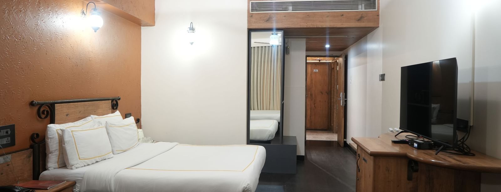 Bedroom with a double bed, a television, and wooden furniture at Infiniti Hotel, Indore.