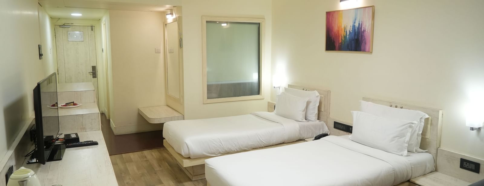 Bedroom with 2 single beds, a television, desk and wall paintings at Infiniti Hotel, Indore.
