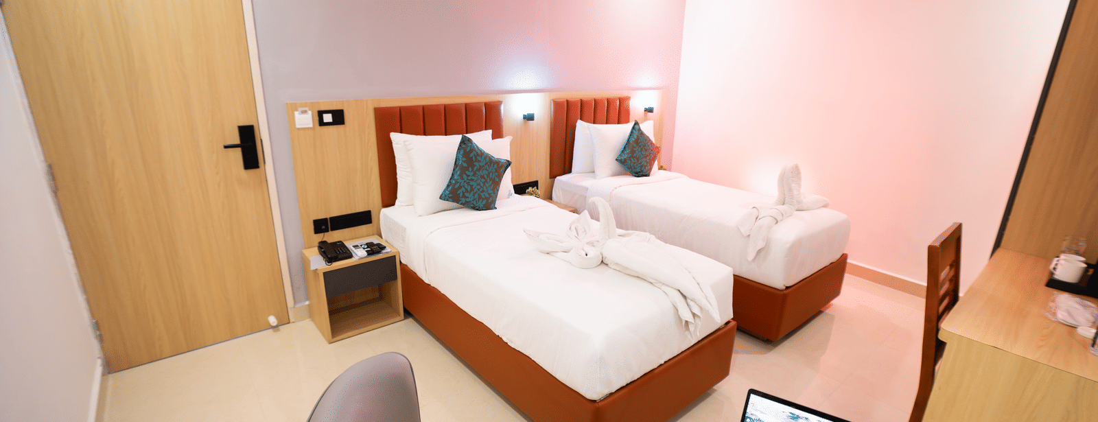 View of a room with twin beds and a laptop on a small round table with chairs on either side at Sunrise Business Hotel, Hyderabad.