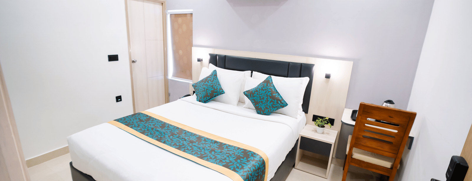 A room featuring a spacious bed, wall-mounted A/C above the headboard, a mirror, and a closed door to the side at Sunrise Business Hotel, Hyderabad.