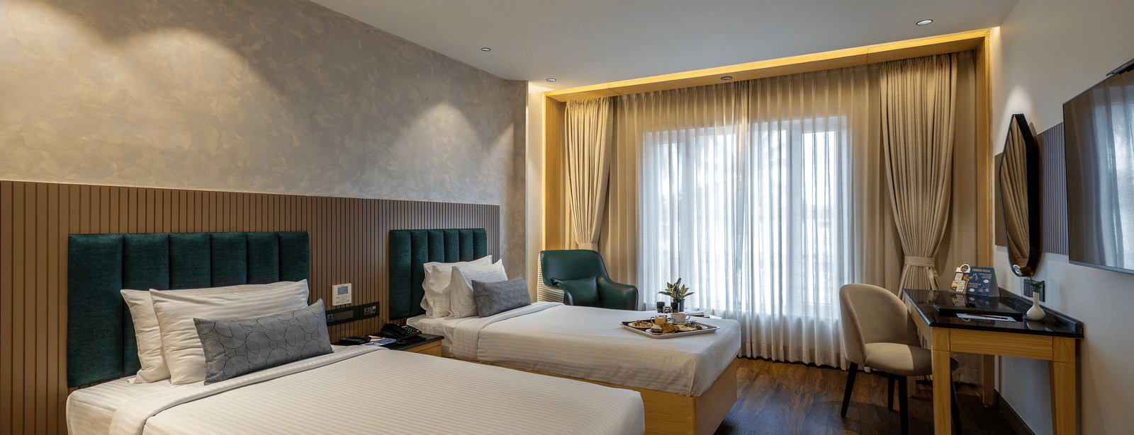 A hotel room at the Citrine Hotel with twin bed, a TV, and a large window with drapes closed.