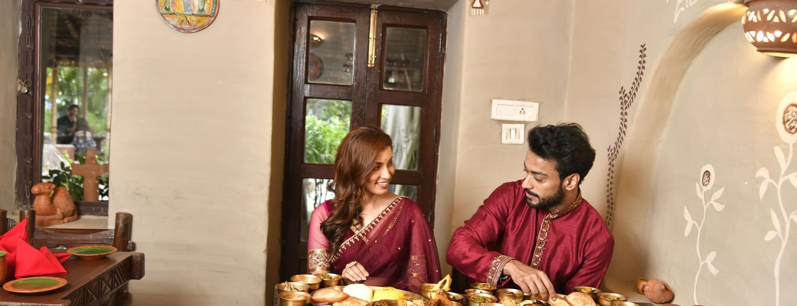 Two people in traditional attire sitting at a low table laden with multiple dishes of food | Bhoomi Restaurant