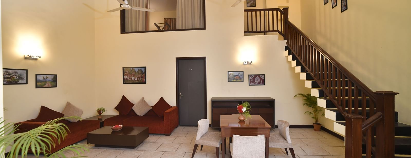 A living room with high ceilings includes a staircase, comfortable sofas, and a dining table set for a meal Green Villas