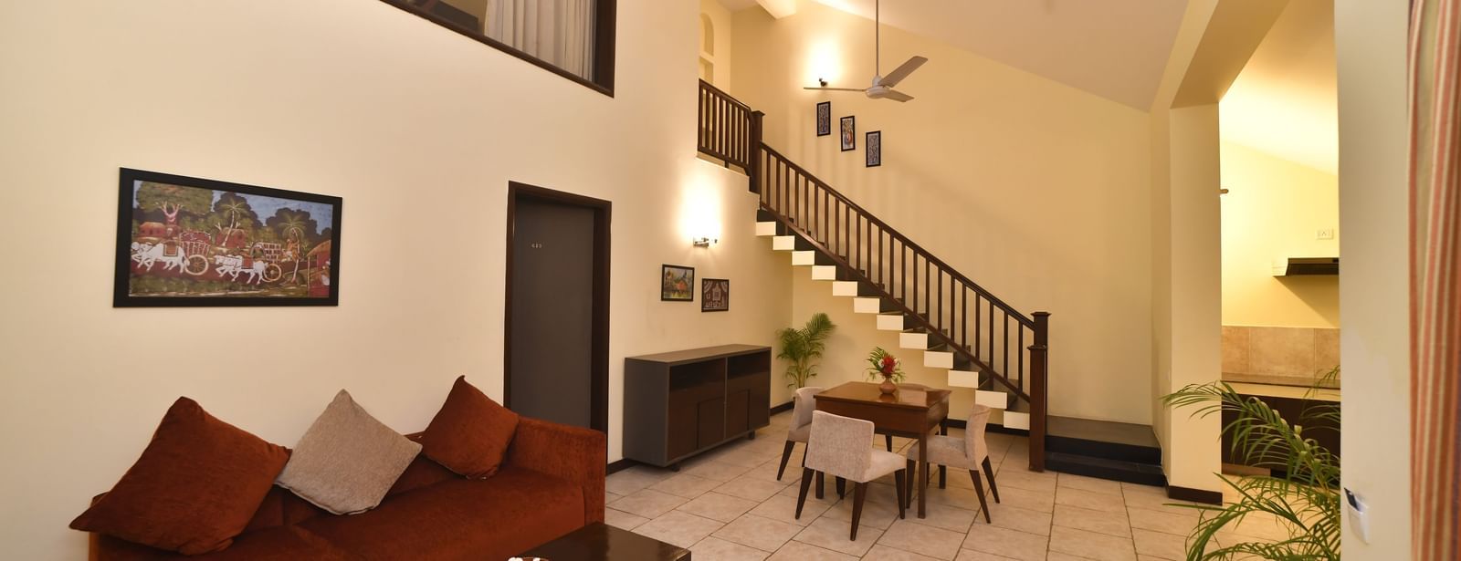 A living room highlights the staircase, a seating arrangement, and a television | Green Villas