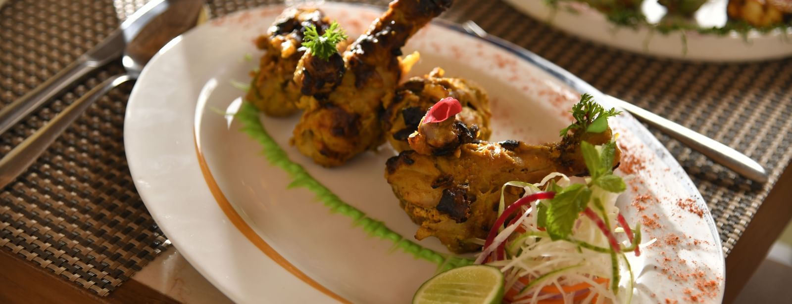 A plate of food with grilled chicken and a lime wedge at Vedic Village Spa Resort.