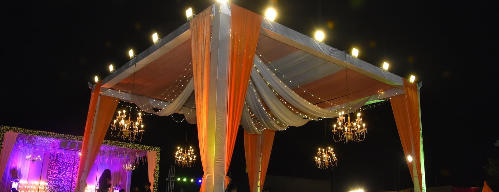 Outdoor event canopy with draped lights and seating at Vedikant Hotels & Resorts with night sky in the background.