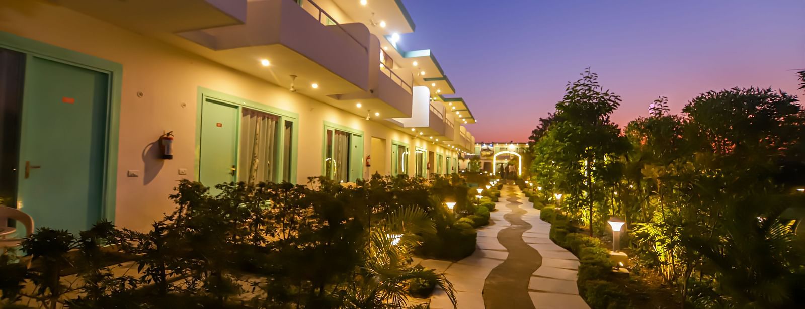 An evening view along a path at Vedikant Resorts The Mallard Corbett shows rooms with lit balconies.