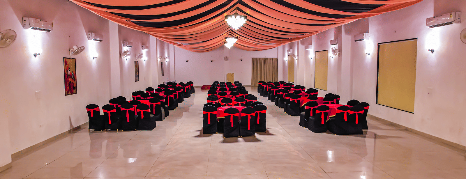 An empty banquet hall at Vedikant Resorts The Mallard Corbett has rows of chairs set up for an event under a decorated ceiling.