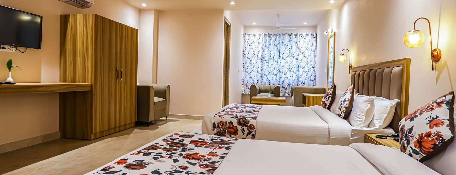 A spacious bedroom at Vedikant Resorts The Mallard Corbett includes multiple beds, a television, and ample lighting.