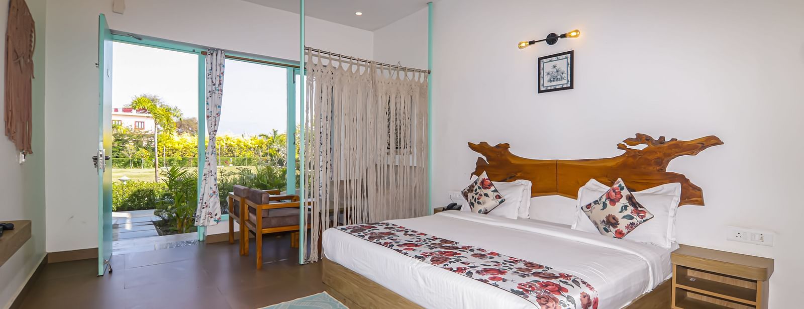 Brightly lit guest room at Vedikant Resorts The Mallard Corbett with a double bed, side table, and garden view through glass doors.