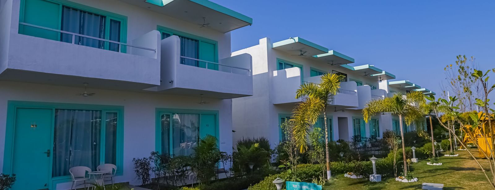 Pathway and building exterior at Vedikant Resorts The Mallard Corbett with trimmed plants, stairs, and room balconies.