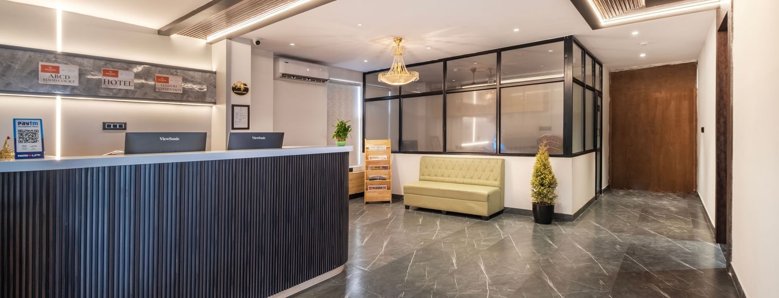 Well-lit hotel reception with modern interiors, seating area, and plant decoration at Monday Hotels Amalapuram Heights
