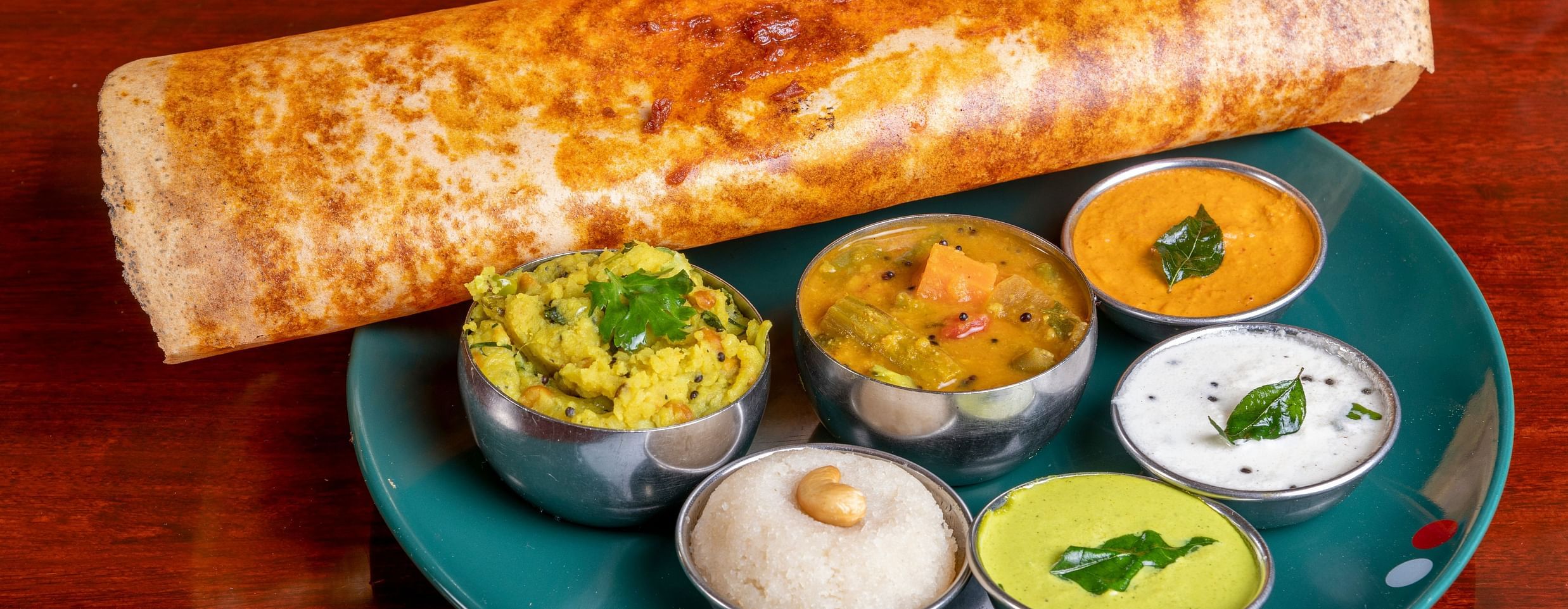 A image of a dosa served on a plate with different side dishes