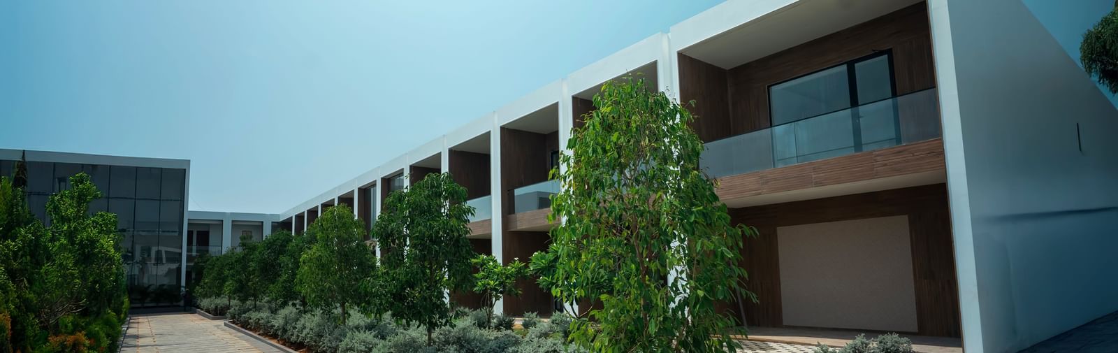 Corner view shot of a two storey building with tropical plants lined in front of it besides a pathway at The Shore Trishvam, Pondicherry.