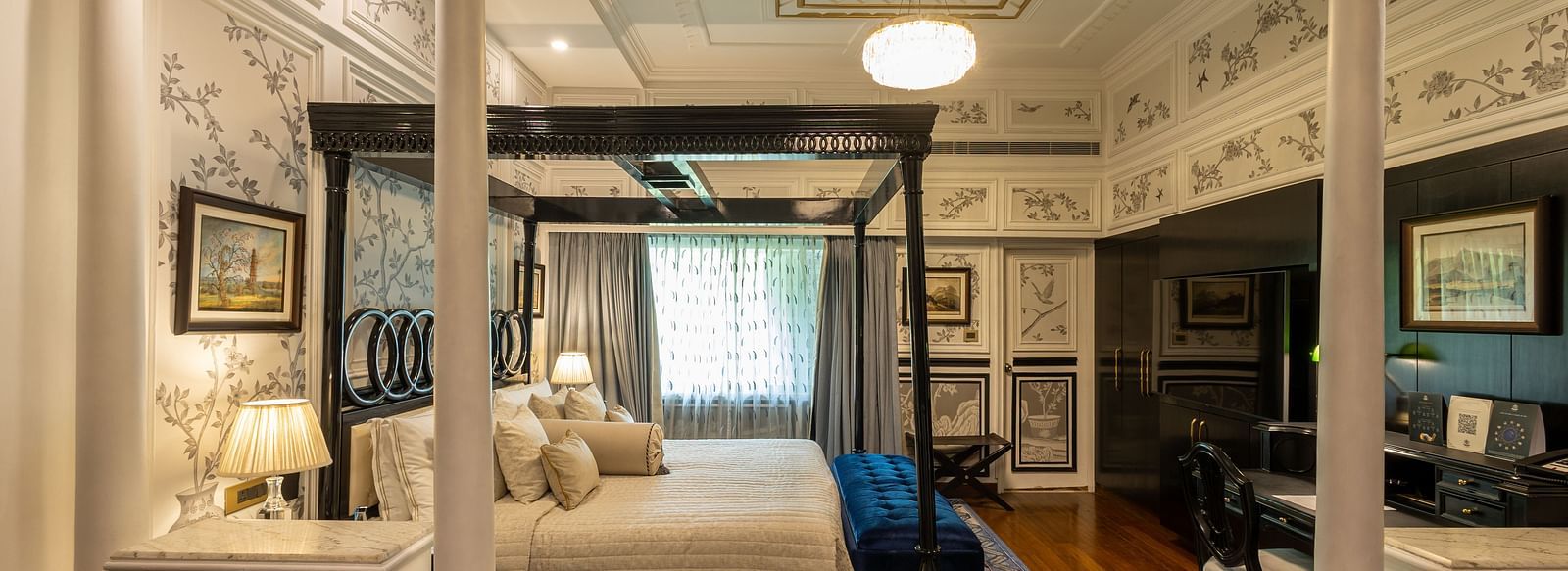 Grand Luxury Room at The Claridges New Delhi, showcasing a side view of the canopy bed with a bedside lamp and a chandelier