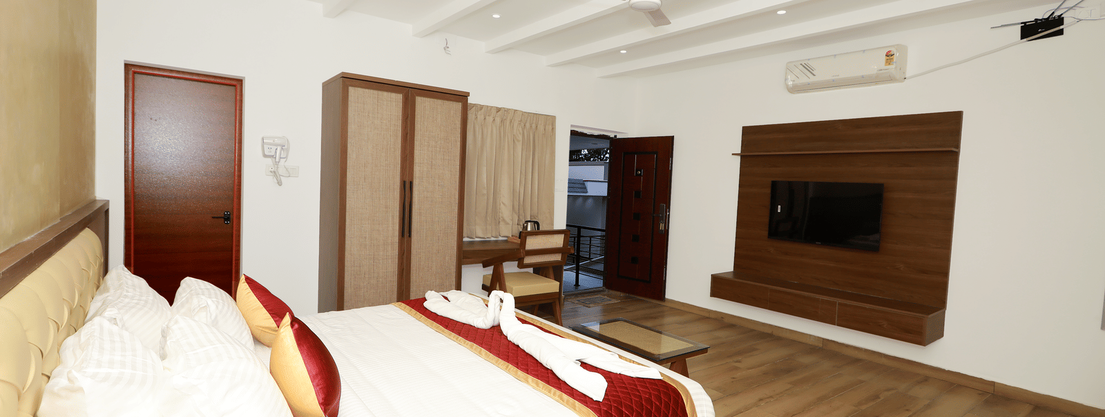 Corner view of the Nature Luxury Room featuring a double bed facing towards the wall-mounted television with the entrance door wide open in the corner at WOW Naturefull Resorts, Yercaud.