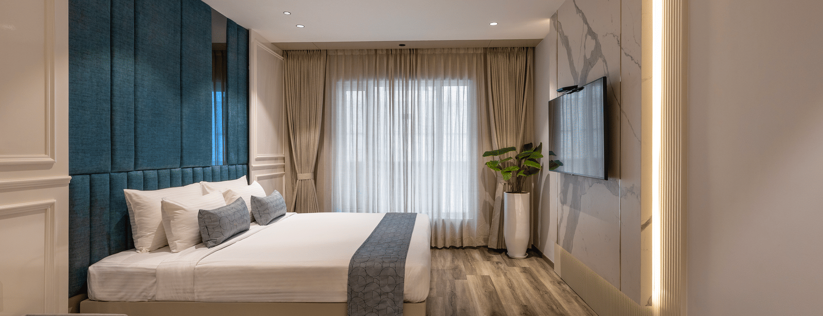 A room at the Citrine Hotel with a bed, a TV mounted on the wall, and a large window.