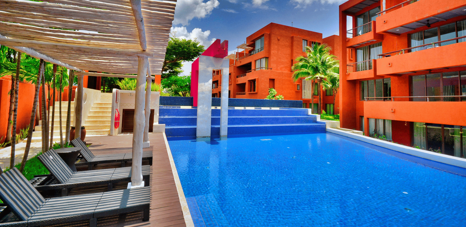 Vibrant hotel facade featuring sun loungers and a pool.