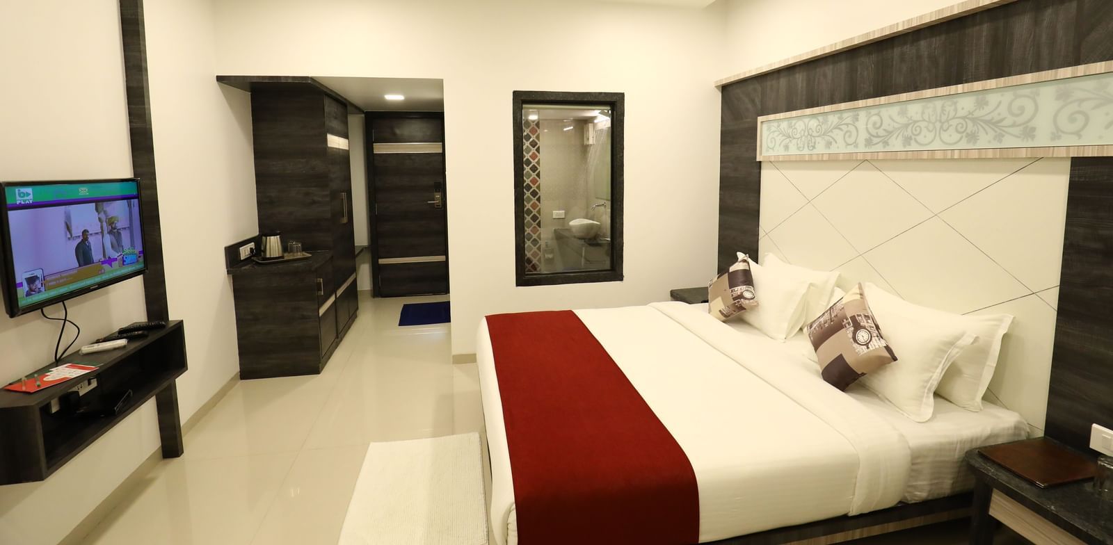 A room in Imperial Grande with a bed covered in white and red bedding, a television on a stand, and a mirror on the wall.