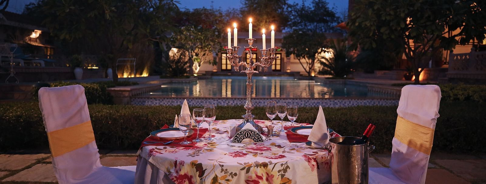 A beautifully set outdoor dining table illuminated at dusk, with buildings in the background - Khas Bagh, Jaipur.