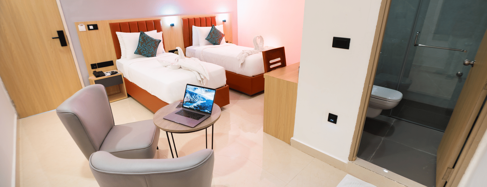 Interior of a room with twin beds, a seating area, and a doorway leading to a bathroom at Sunrise Business Hotel, Hyderabad.