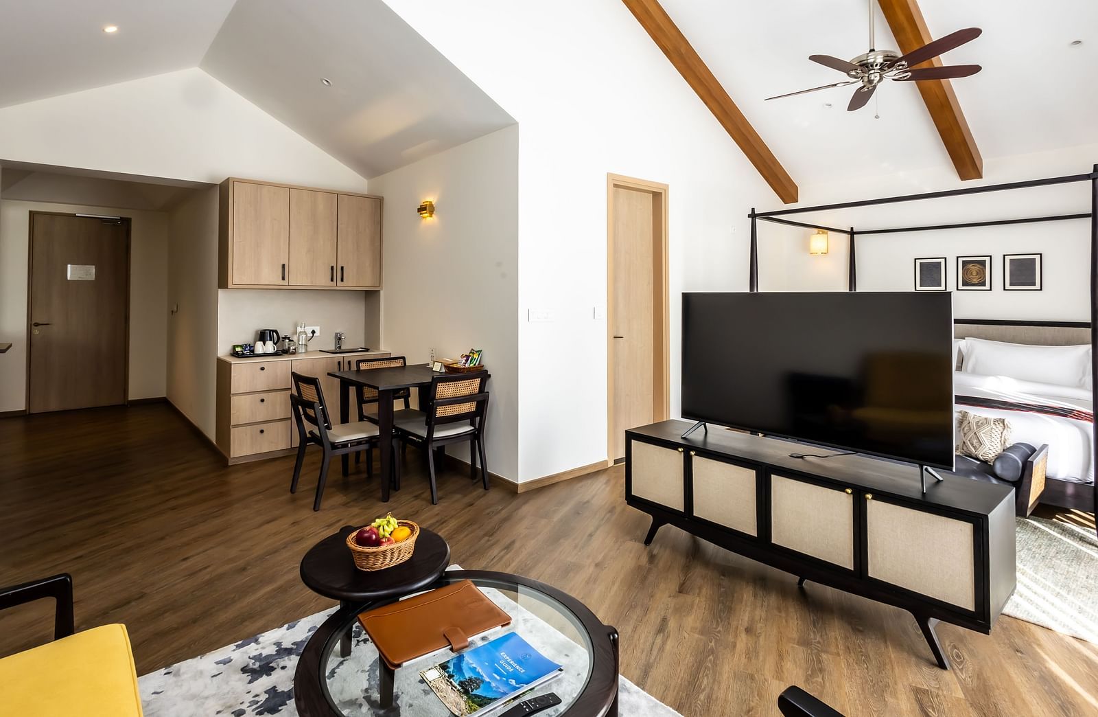 A suite featuring a four-poster bed, television, kitchenette, dining table, a coffee table, and a glimpse of the sofa in a bright ambience at Nivasana Manali.