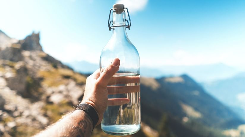 A person holding a reusable glass water bottle amidst mountains