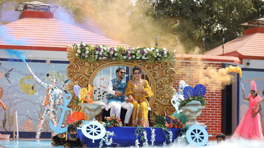 A couple sitting on a decorated chariot float positioned at the edge of a pool at Amantra Shilpi Resort, Udaipur.
