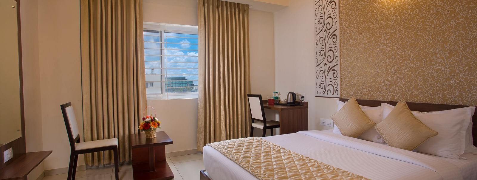 A hotel room with a comfortable bed, a wooden side table with flowers and a city view through the window - De Venetian by TGI, Brookefield