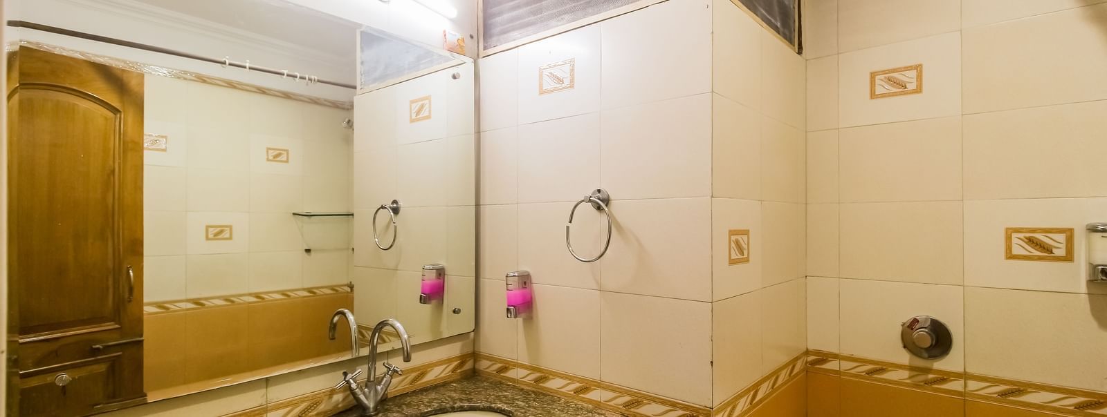 A bathroom with a white oval sink, a granite countertop, a toilet, and a tiled wall with a mirror, illuminated by a light fixture. - Hotel Diamond Plaza, Chandigarh.