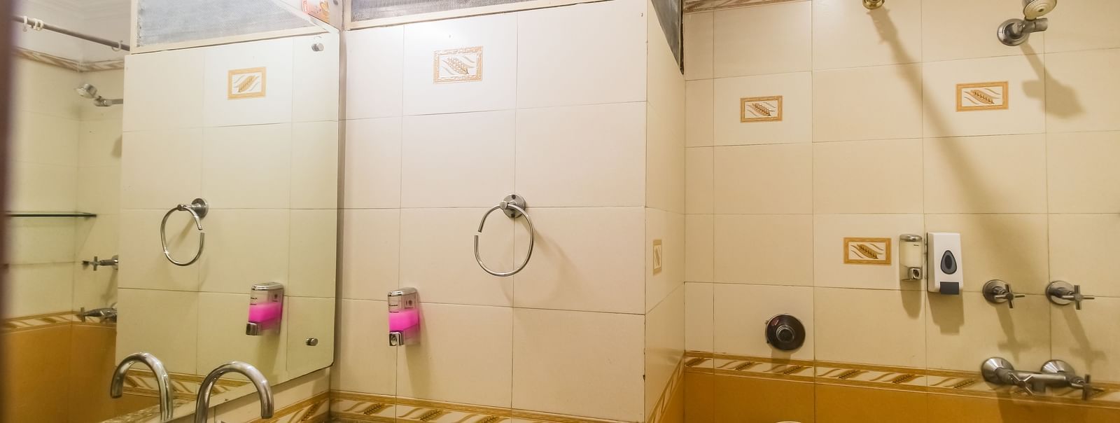 A bathroom with a white oval sink, a granite countertop, a toilet, and a tiled wall with a mirror, illuminated by a light fixture. - Hotel Diamond Plaza, Chandigarh.