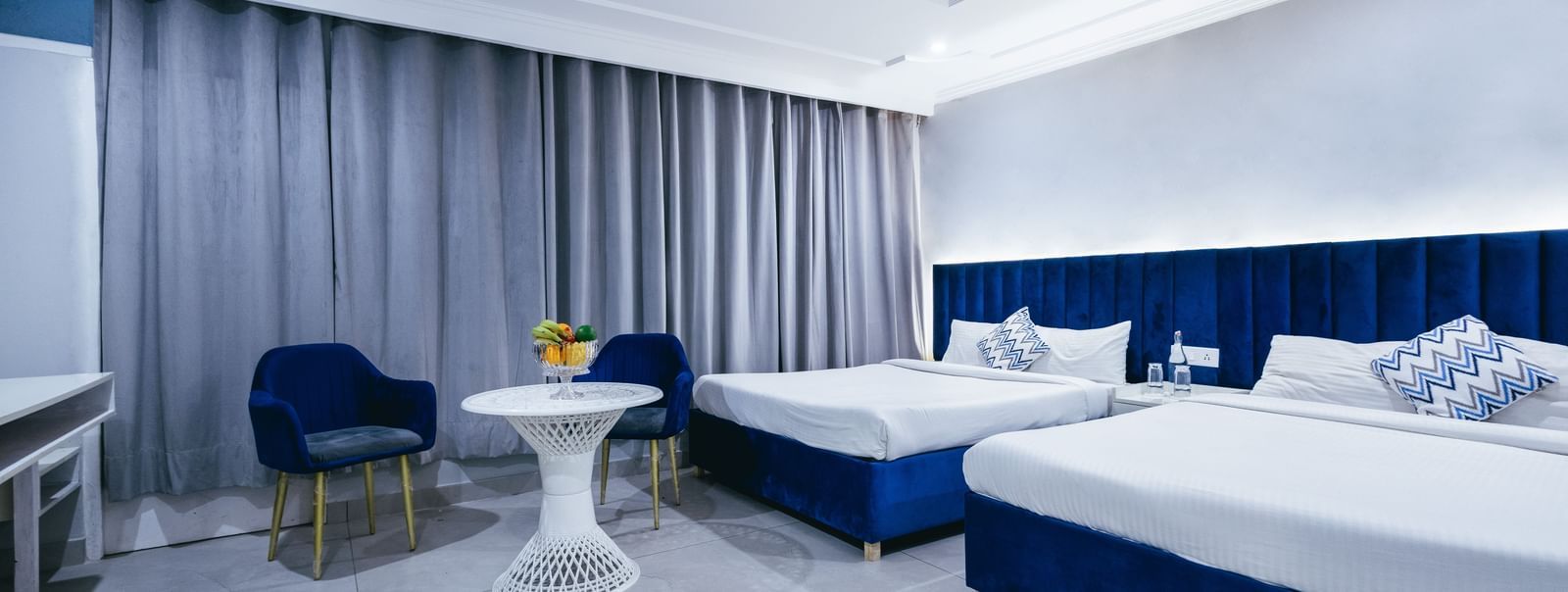 Bright, spacious family room with a two large sized bed, work desk, and full-length curtains at Hotel Downtown17, Chandigarh.