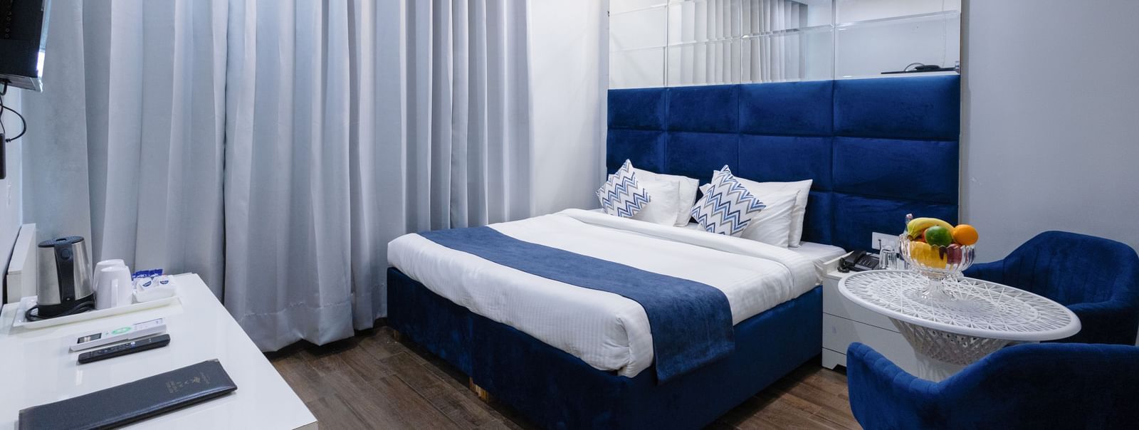 Hotel Room  at Hotel Downtown17, Chandigarh featuring a king size bed with a blue headboard and white and blue linens, two blue chairs with a small round table, and light wood-look flooring. 