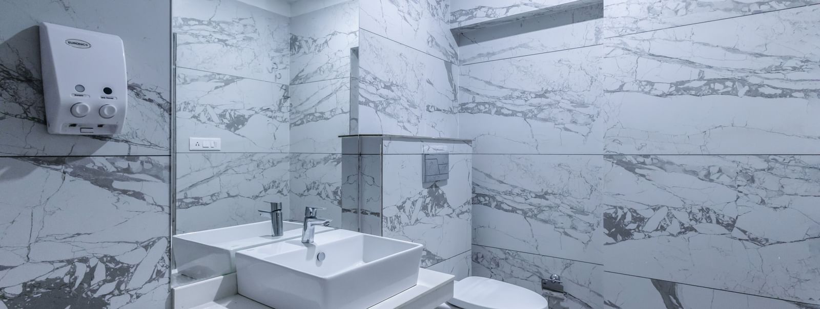 Modern bathroom with a white sink, mirror, toilet and elegant textured textiles at Hotel Downtown17, Chandigarh.