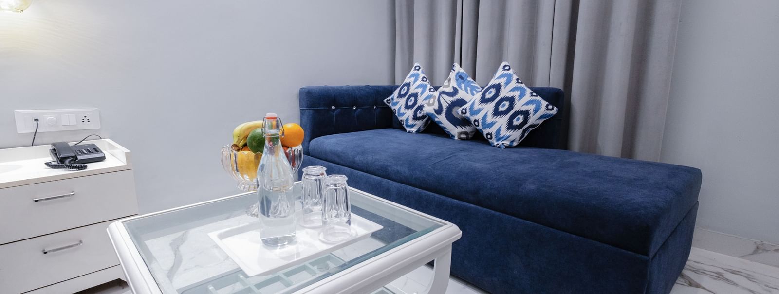Modern living room with a blue couch, patterned pillows, white coffee table at Hotel Downtown17, Chandigarh.and floor-length curtains.