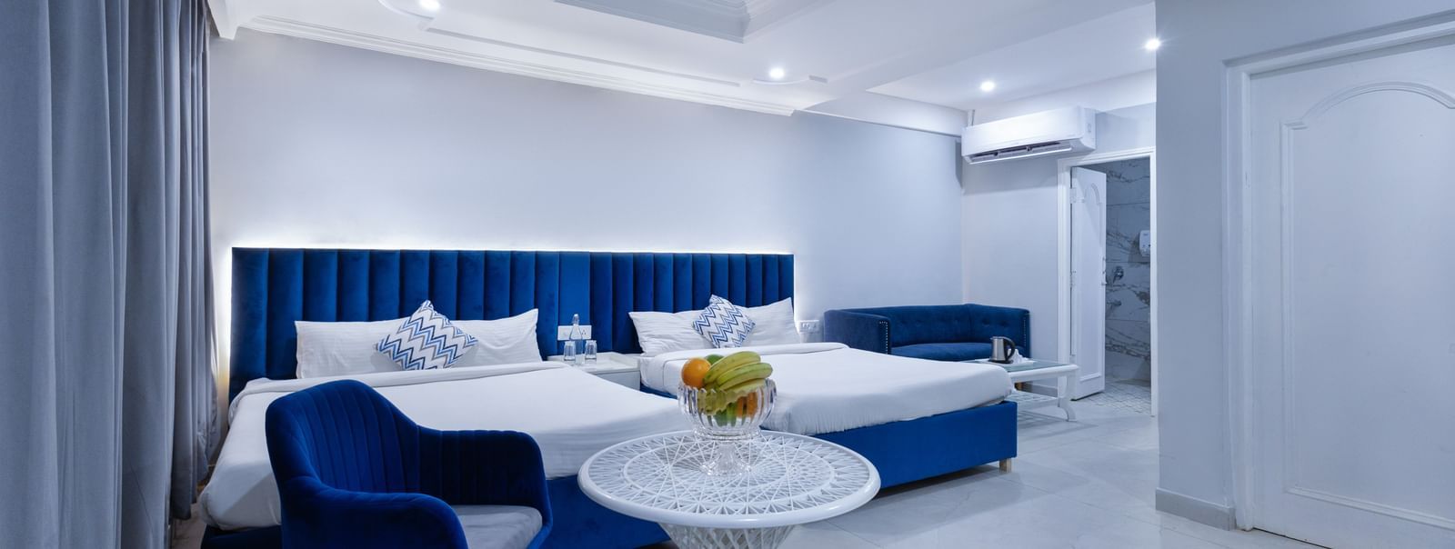 Family room featuring two large beds, a white table with a fruit plate, and a clean, modern interior at Hotel Downtown17, Chandigarh.