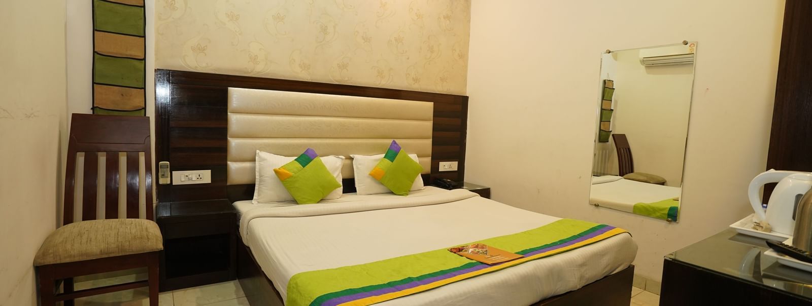 Standard Room in Hotel Dreamland, Chandigarh with food menu placed on the neatly made king-size bed, single chair. 