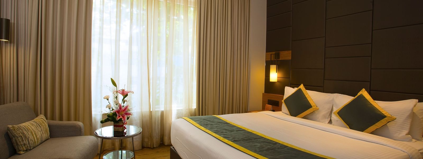 a bedroom with a large bed and a sofa opposite the the bed, with a small table in the middle - Hotel Fountain Tree By TGI - JP Nagar, Bangalore