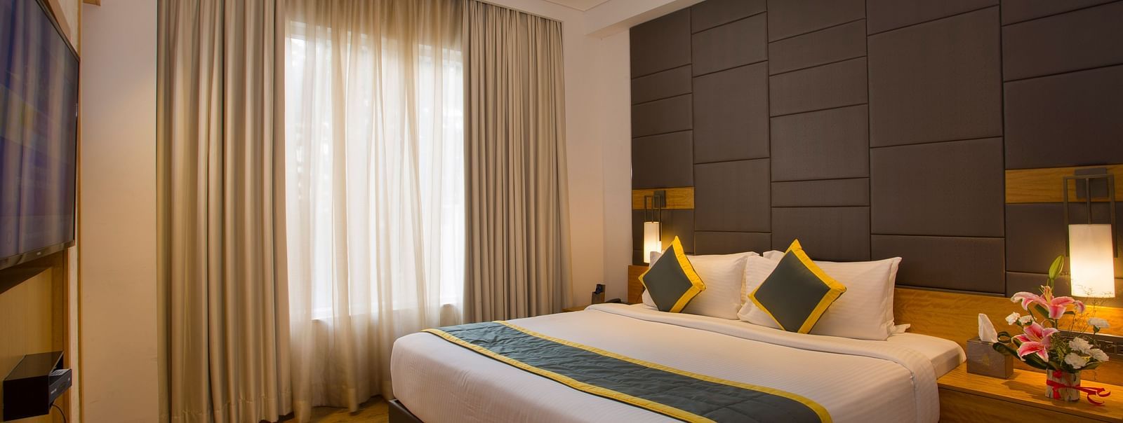 a bedroom with a large bed opposite a television mounted on the wall and side drawers on each side - Hotel Fountain Tree By TGI - JP Nagar, Bangalore
