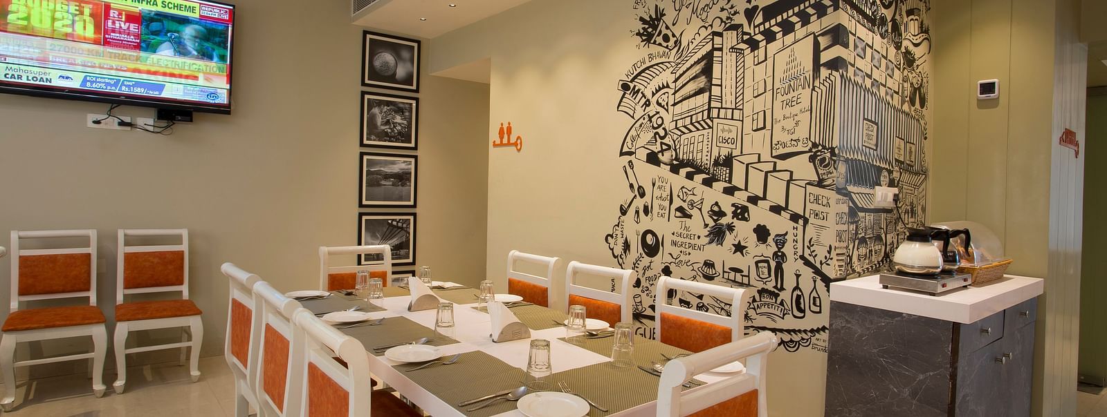 A cosy restaurant corner with a large wall mural, a buffet counter and a flat-screen TV showing news - Hotel Langford Keys by TGI, Shanti Nagar