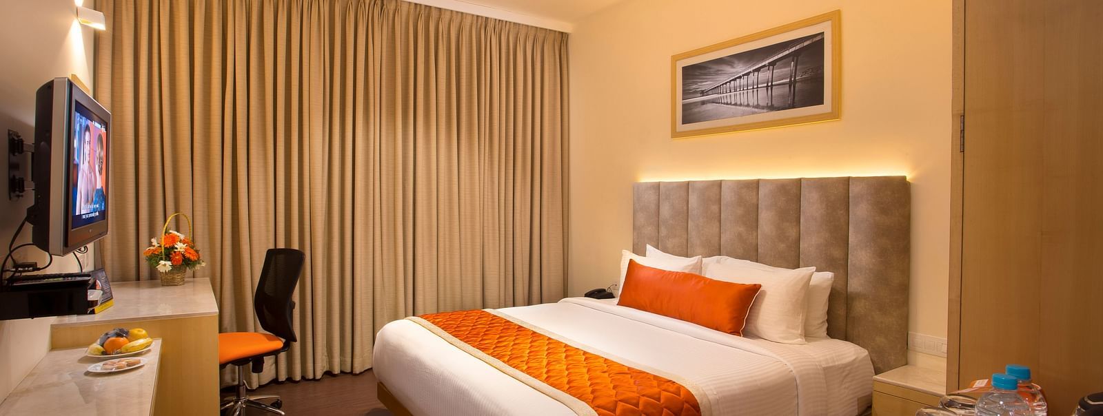 A cosy hotel room with a plush bed adorned with an orange bed runner, a work desk and a wall-mounted TV - Hotel Langford Keys by TGI, Shanti Nagar