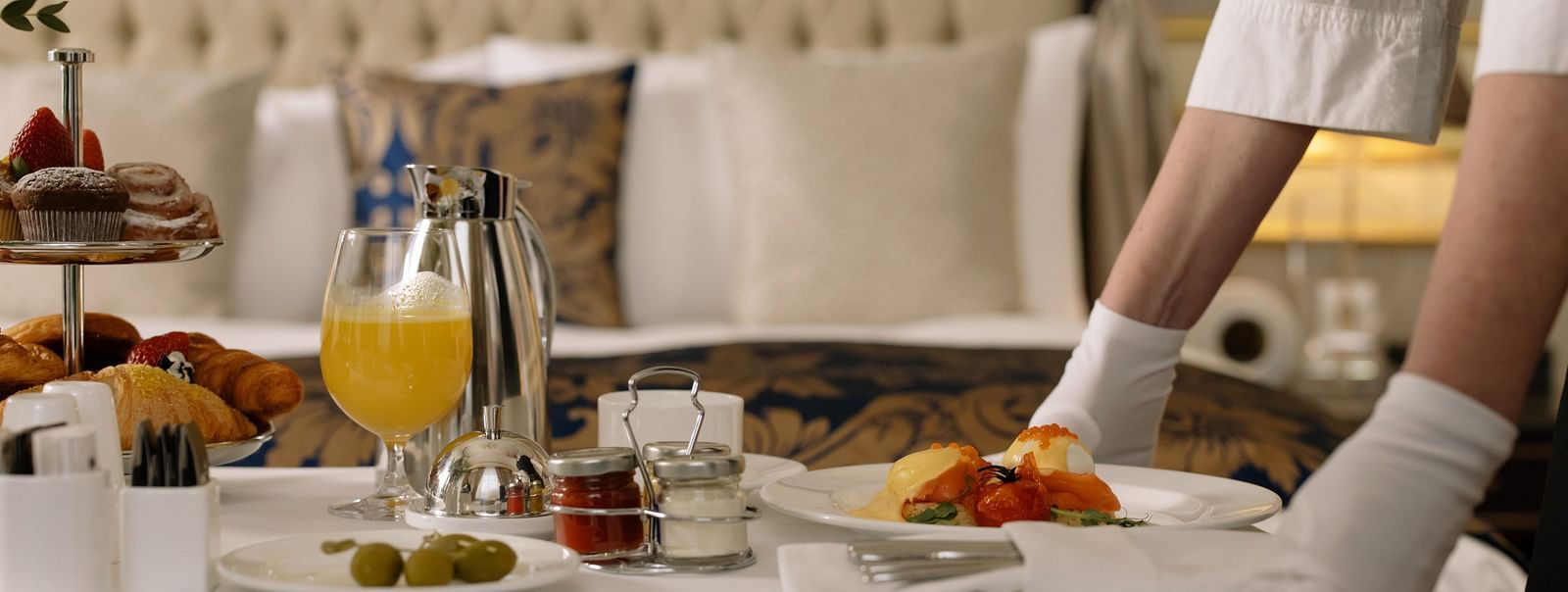 A room service attendant serving breakfast with eggs and pastries on a bed