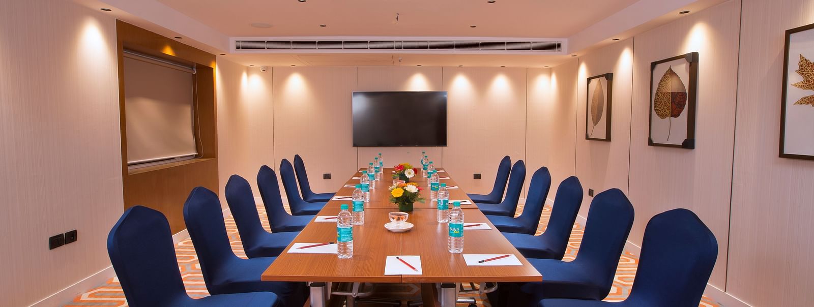 A well-lit boardroom with a long table, blue chairs and a large screen on the wall, suitable for business meetings - Hotel Southend by TGI - Bommasandra, Bangalore
