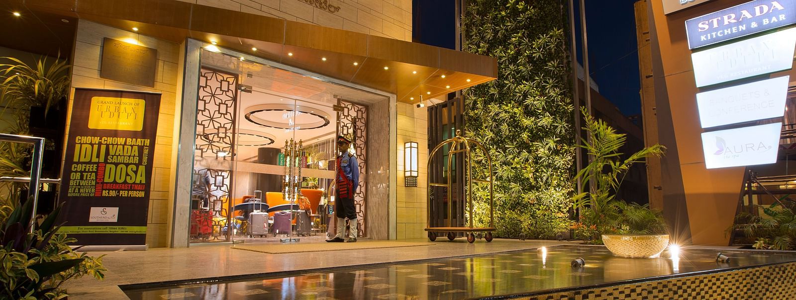 The exterior entrance of a hotel at dusk, featuring signage, a bellhop and a reflective water feature - Hotel Southend by TGI - Bommasandra, Bangalore