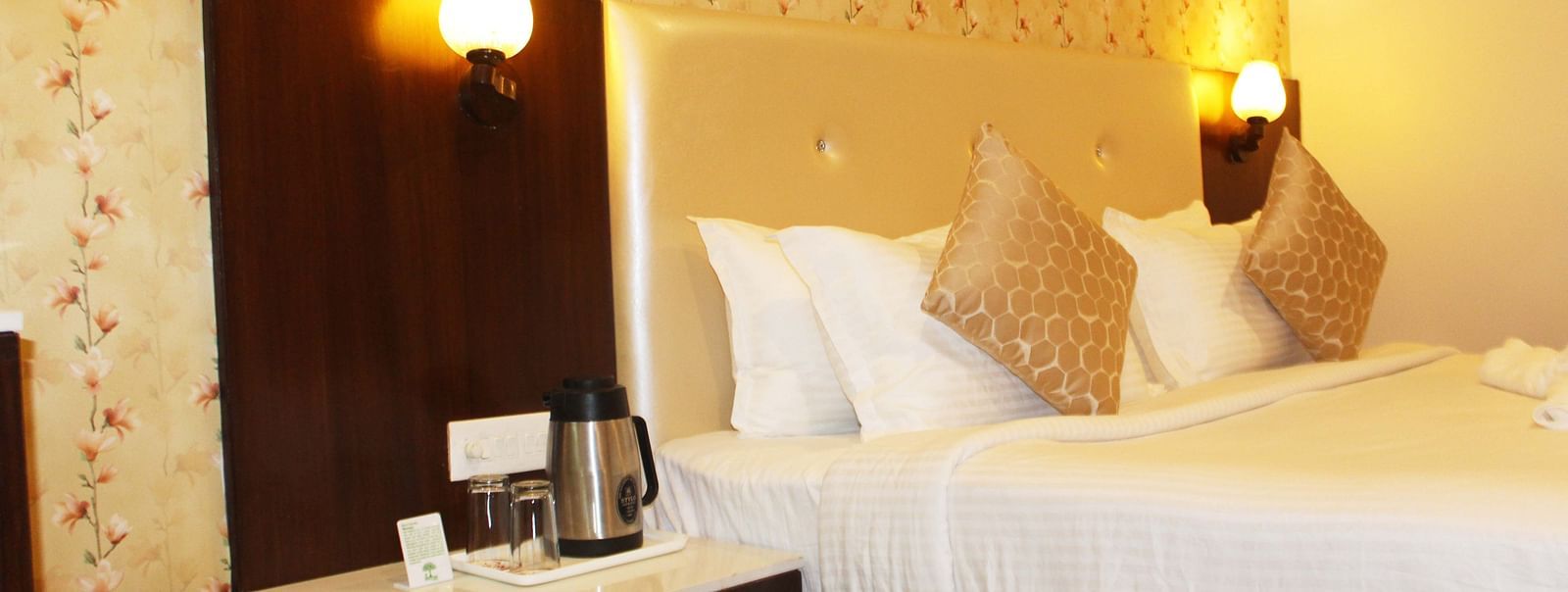 A hotel room with a beige headboard, white linens, floral wallpaper and a coffee-making station - TGI Apple Inn, Jaipur 