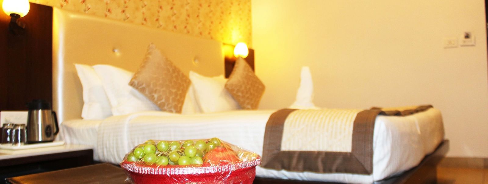 A hotel room featuring a bed with white linens, a brown runner and a bowl of fruits on the table - TGI Apple Inn, Jaipur 