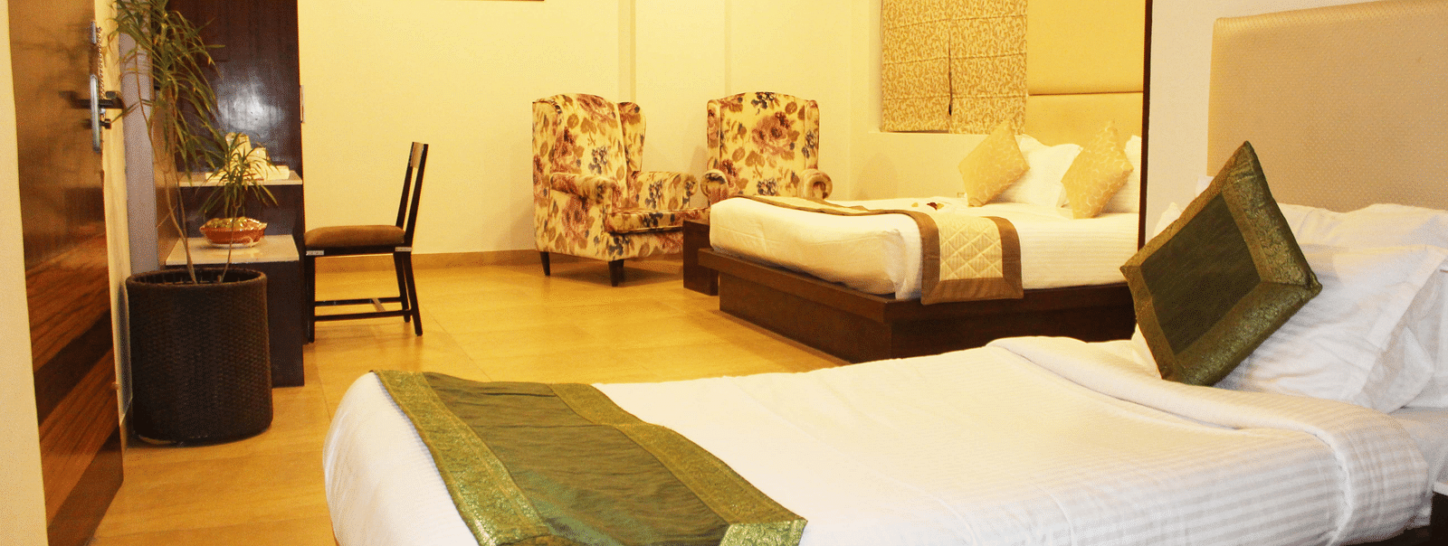 Another view of a spacious hotel room with two armchairs, a large bed with white linens and patterned wallpaper - TGI Apple Inn, Jaipur 