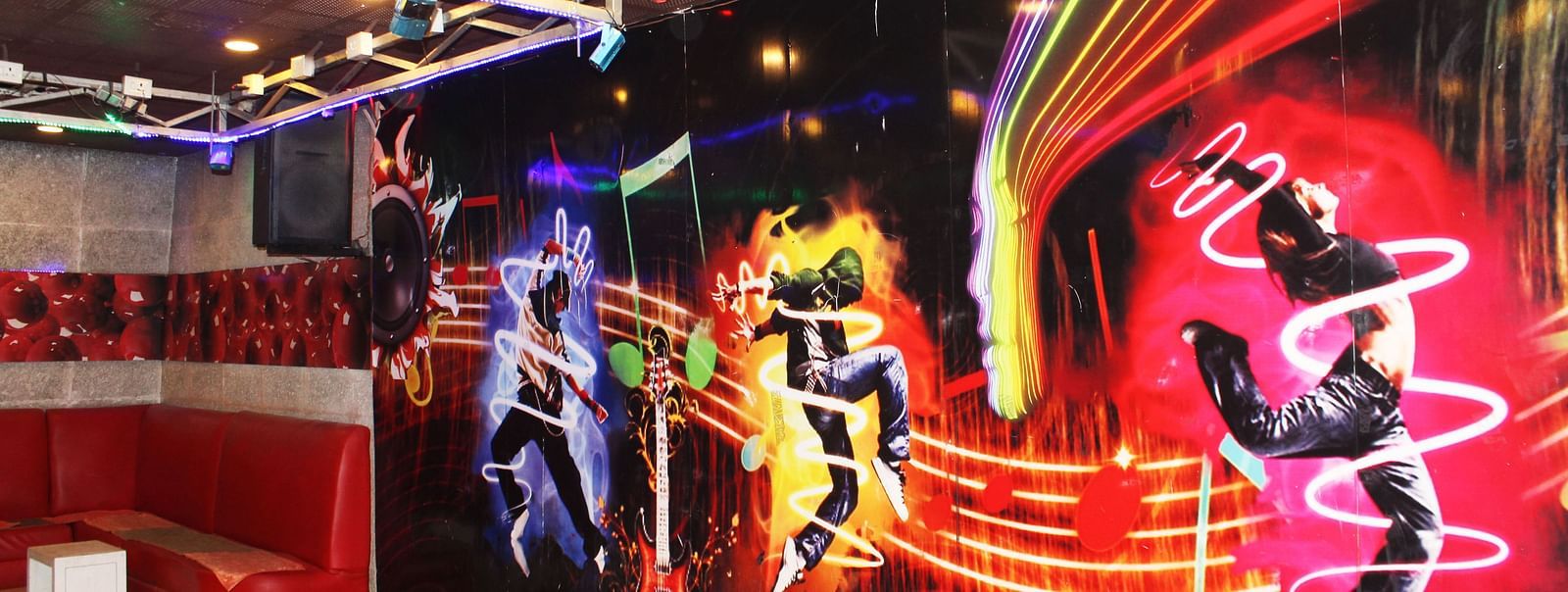 A dance club with vibrant wall murals of dancers, a red tufted sofa and disco lighting - TGI Apple Inn, Jaipur 
