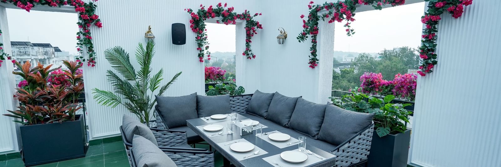 A wide angle shot of a dining table with a capacity of 6 people featuring a white coloured wall behind it at the Sky Roof during the day at M2 Square by Monday Premium.